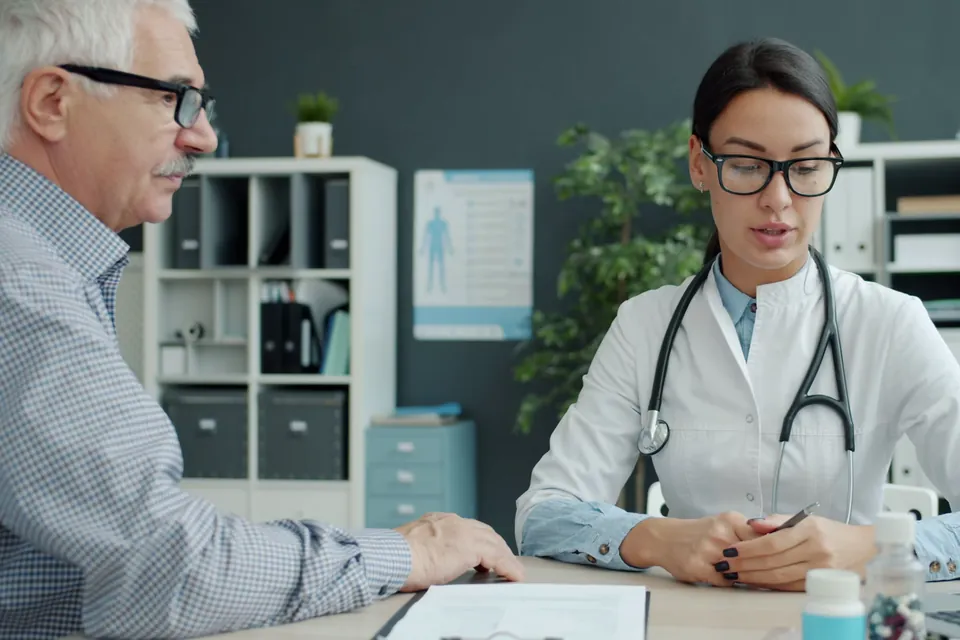 Illustrative stock photo: a clinician in a white coat reviews notes with an older patient in an office.